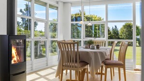 A room with a fireplace, a dining table with chairs, and large windows offering a view of greenery. - Gorgeous home in Otterup with WiFi (Otterup)