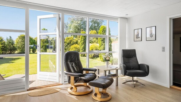 A spacious room with a large sliding glass door leading to a garden, two leather chairs, a small table, and a framed picture on the wall. - Gorgeous home in Otterup with WiFi (Otterup)