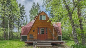 A wooden cabin with a red roof, a front door, and a porch with steps leading up to it. - Gateway to Glacier (Columbia Falls)