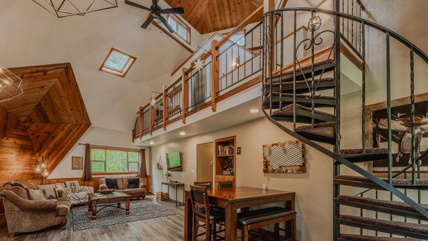 A spacious loft-style living area with a high ceiling, wooden floors, a central seating area with a sofa and chairs, a dining table, and a spiral staircase. - Gateway to Glacier (Columbia Falls)
