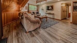 A spacious loft-style living area with a high ceiling, wooden beams, a staircase, and a large window. - Gateway to Glacier (Columbia Falls)