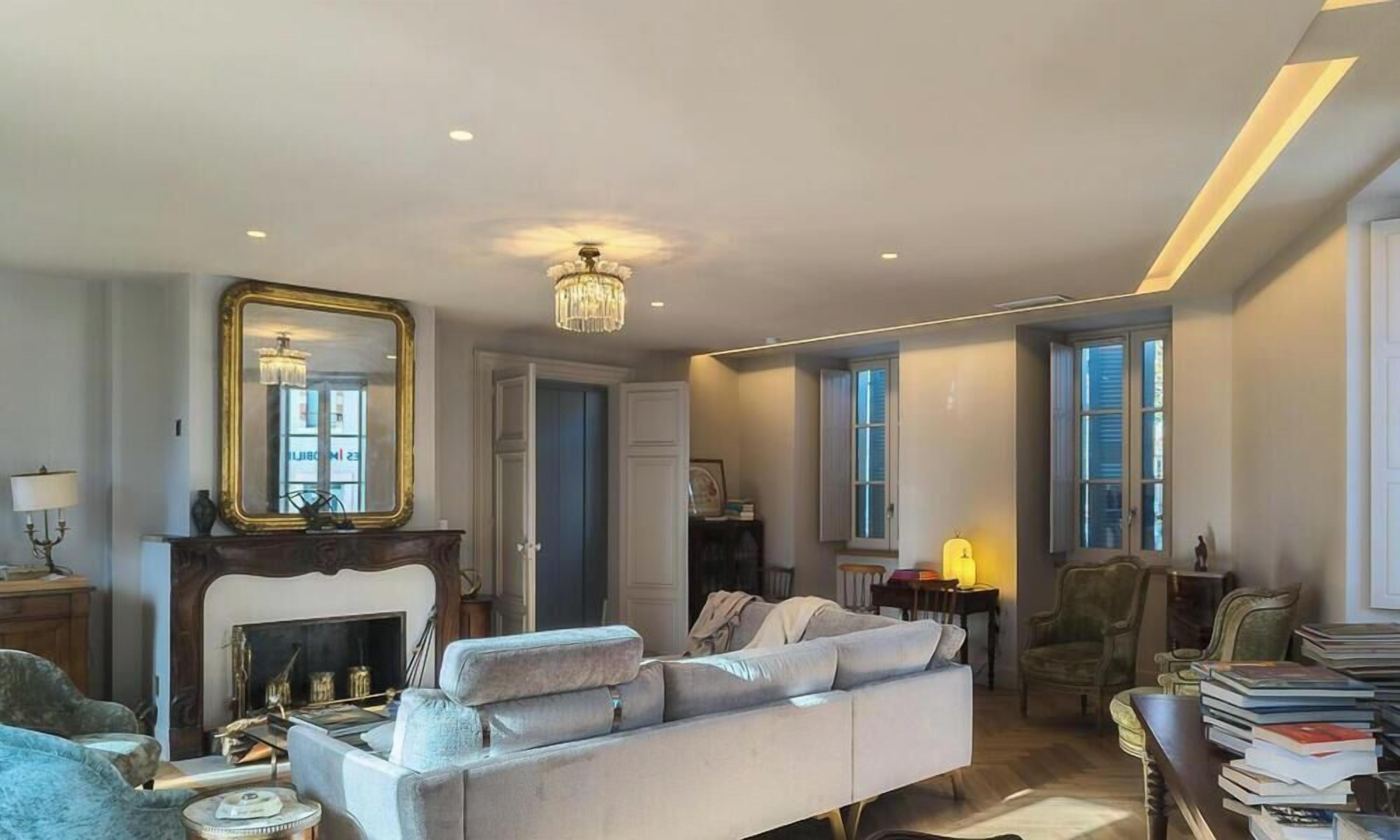 Un salon avec une cheminée, un grand miroir, un lustre et un canapé.