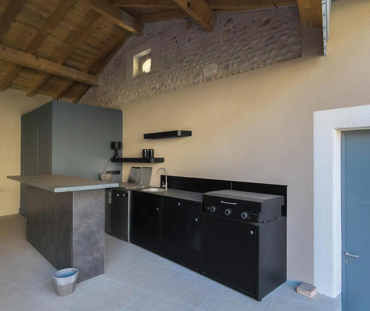 Une cuisine moderne avec un mur en pierre, un îlot central intégré et une porte sur le côté droit.