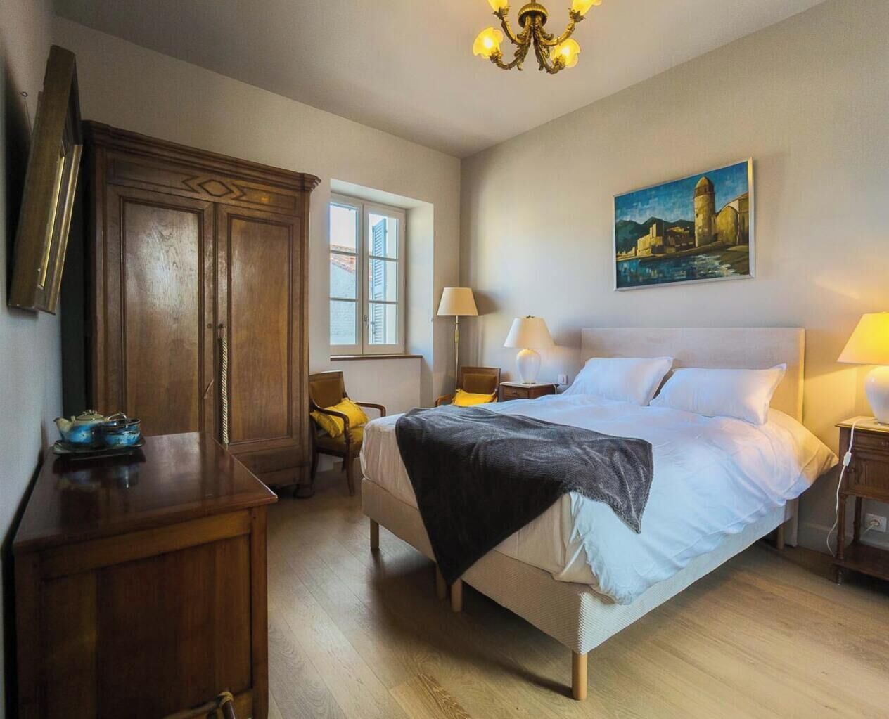 Une chambre à coucher avec un lit, des tables de chevet, un bureau, une chaise, une armoire, une fenêtre et un tableau au mur.