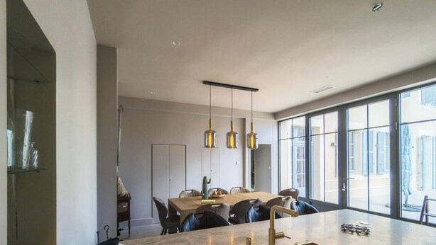 Una cocina moderna con una isla grande, luces colgantes y vistas amplias a través de ventanas.