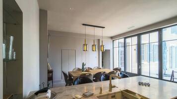 Une cuisine moderne dotée d’un grand îlot central, de luminaires suspendus et offrant une vue dégagée grâce à de grandes fenêtres.