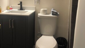 Un baño con inodoro, lavamanos, espejo y un cubo de basura.