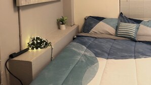 Un dormitorio con cama, un cuadro en la pared, una planta pequeña y una ventana con persianas.