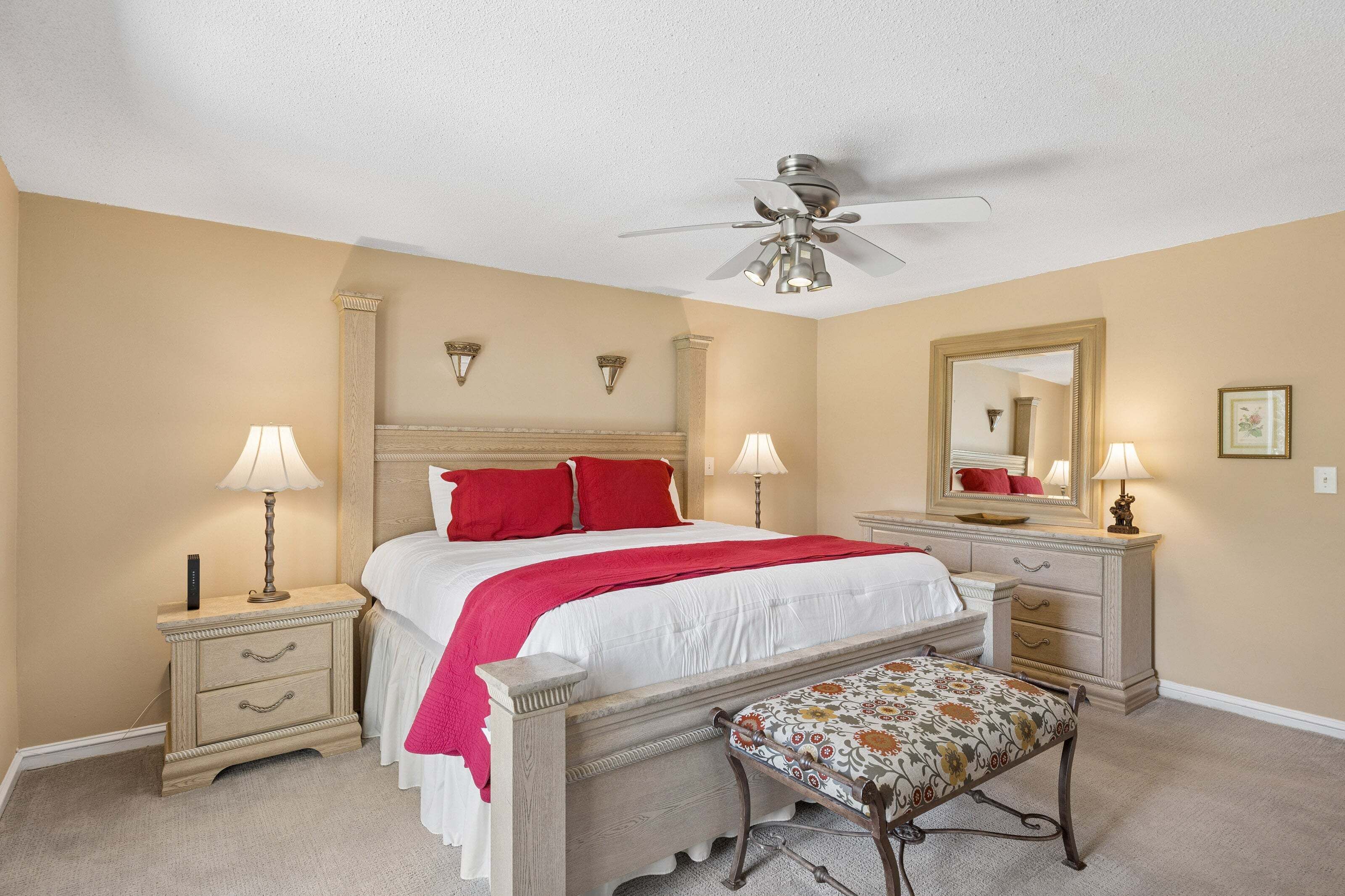 A bedroom with a bed, bedside tables, a bench, a ceiling fan, a dresser, and a mirror.