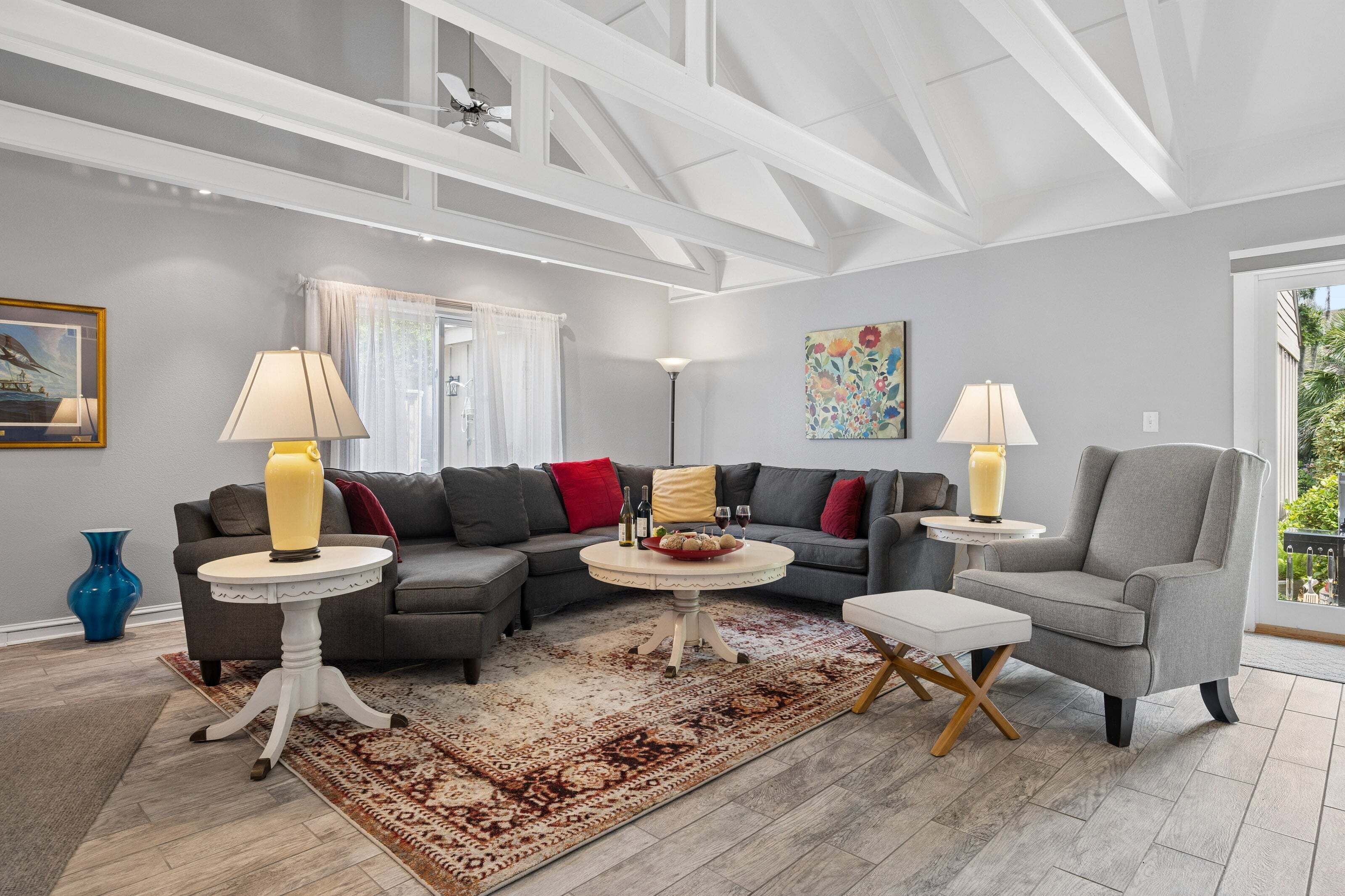 A modern living room with a sectional sofa, two side tables, a patterned rug, and a ceiling with exposed beams.