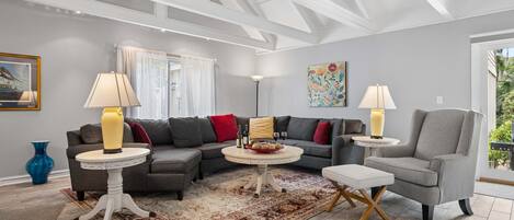 A modern living room with a sectional sofa, two side tables, a patterned rug, and a ceiling with exposed beams.