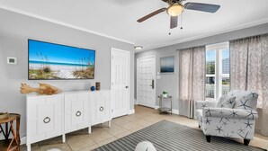 Ein Zimmer mit Deckenventilator, einem großen Fernseher, einem weißen Schrank, einem gemusterten Sessel und Meerblick.