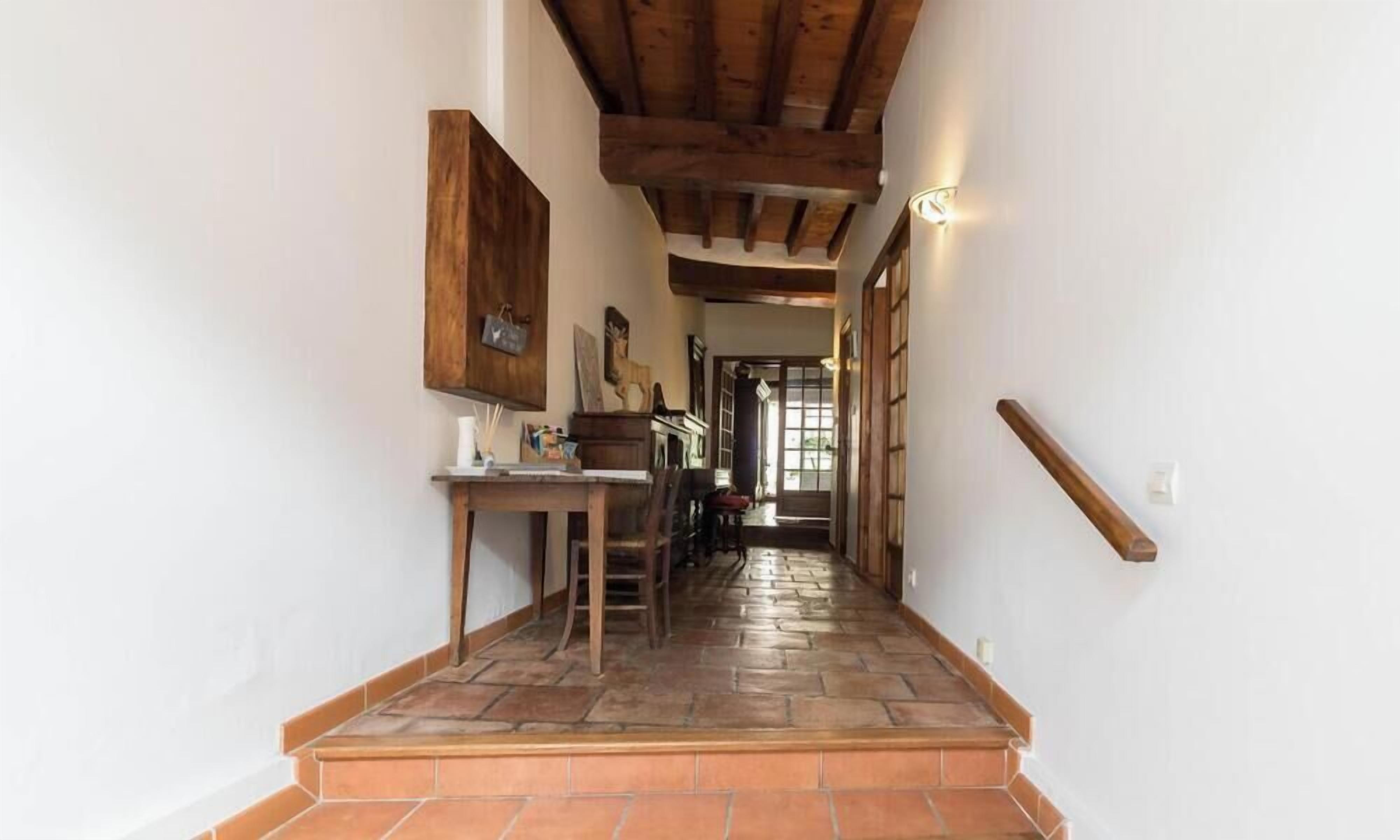 A hallway with a wooden ceiling, a tiled floor, and a staircase leading to another room.