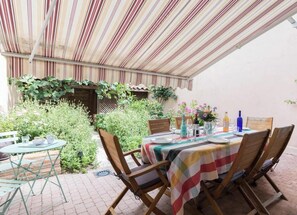 An outdoor patio with a table set for dining, surrounded by greenery and a striped awning. - La Casa de Mamita - FRONTON (FRONTON)
