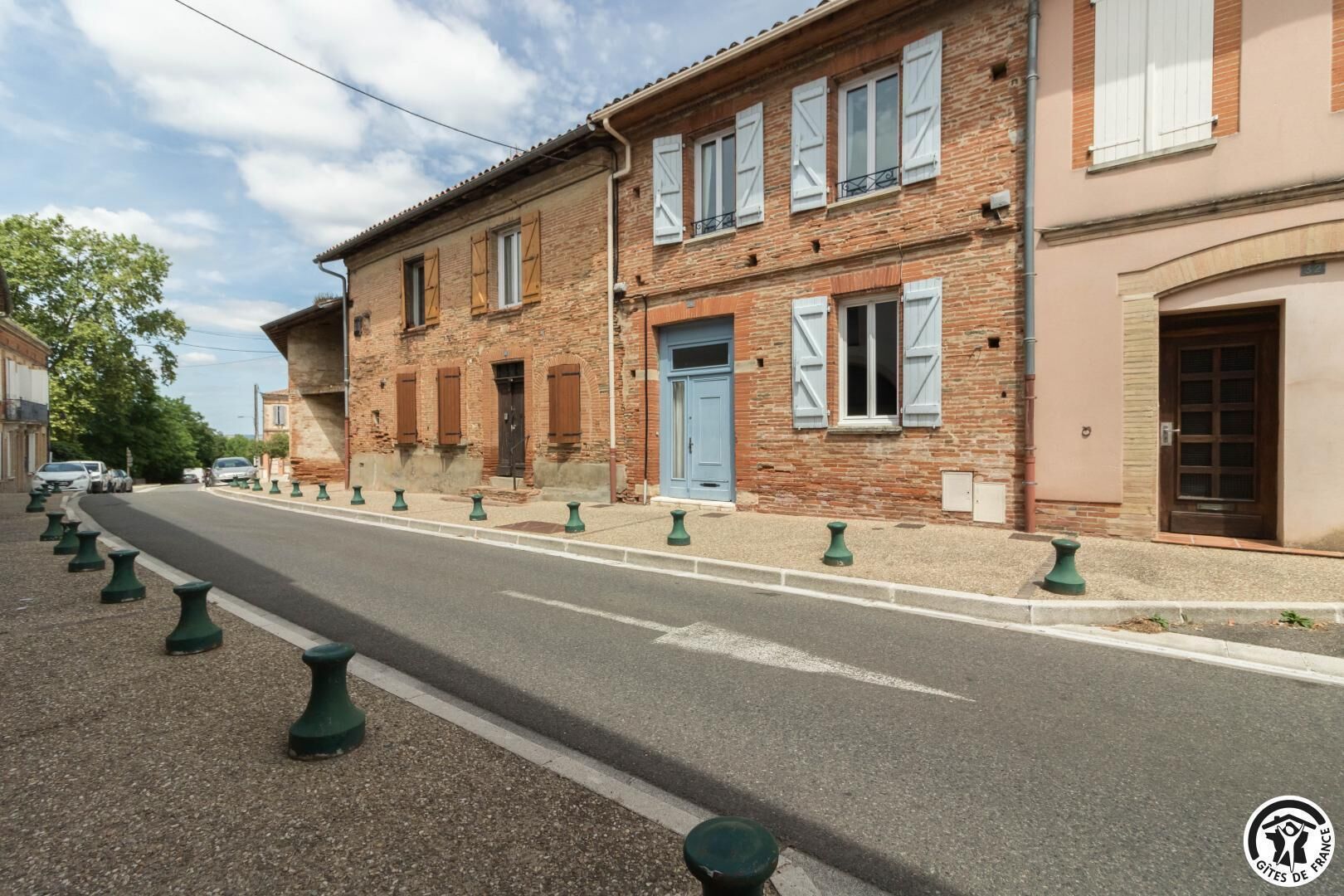 A street with a row of traditional brick buildings, a blue door, and green bollards lining the road.