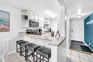 Eine moderne Küche mit weißen Schränken, einer Granit Arbeitsplatte und einer eingebauten Mikrowelle. Es sind drei schwarze Barhocker und ein weißer Stuhl vorhanden.