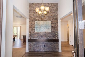 A stone fireplace with a chandelier, a framed abstract painting, and a wooden bench. - Family Escape to Sunset Paradise (Santa Clara)