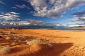 A desert landscape with sand dunes and a distant body of water under a partly cloudy sky. - Family Escape to Sunset Paradise (Santa Clara)
