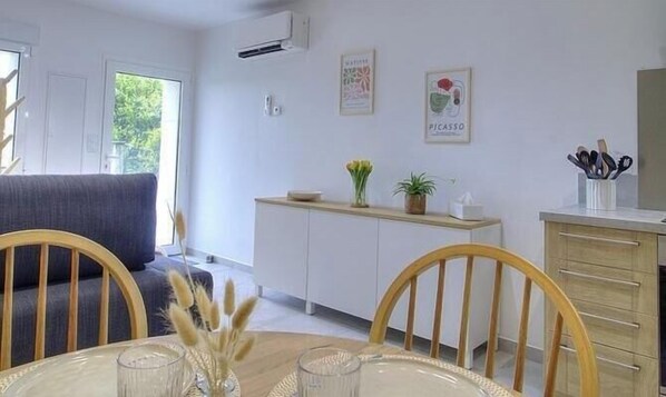 Una cocina moderna con armarios blancos, una mesa de comedor con sillas y una pequeña encimera con una planta y utensilios.