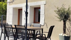 An outdoor patio with a table and chairs, a large umbrella, and a potted plant. - Gîte du Fort - LEAZ - Gîte (LEAZ)