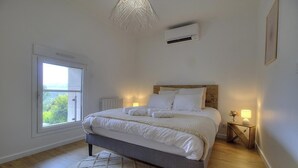 A bedroom with a bed, bedside lamps, a window, and an air conditioning unit. - Gîte du Fort - LEAZ - Gîte (LEAZ)