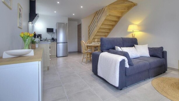 A modern kitchen with a dining area, a grey sofa, and a staircase. - Gîte du Fort - LEAZ - Gîte (LEAZ)