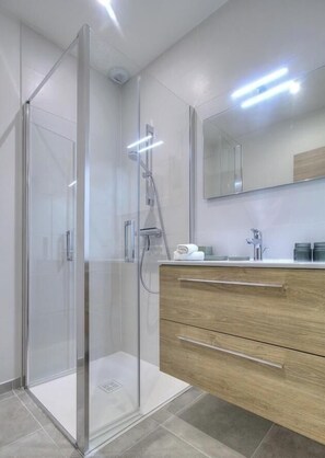Une salle de bain moderne avec une douche à parois de verre, un meuble-lavabo en bois doté de tiroirs et un grand miroir au-dessus du meuble-lavabo.