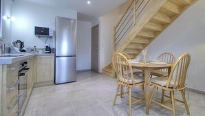 A modern kitchen with a built-in refrigerator, wooden dining table, and chairs. - Gîte du Fort - LEAZ - Gîte (LEAZ)