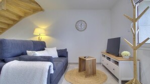 A modern living room with a sofa, a TV, a wooden sideboard, a clock, and a lamp. - Gîte du Fort - LEAZ - Gîte (LEAZ)
