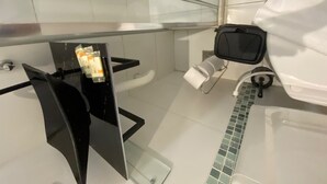 A bathroom with a glass partition, a black chair, a toilet, and a shower area. - Studio Copa Beach (Rio de Janeiro)