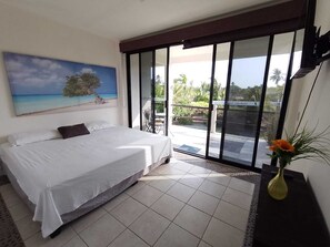 A bedroom with a bed, a painting of a beach, a sliding glass door to a balcony, and a vase with flowers. - Zana Town Bungalows (Barra de Potosi)