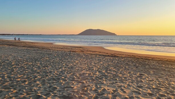 Una spiaggia con un'isola all'orizzonte, mare calmo e impronte sulla sabbia.
