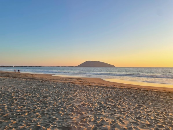 A beach with a distant island, calm sea, and footprints in the sand. - Zana Town Bungalows (Barra de Potosi)