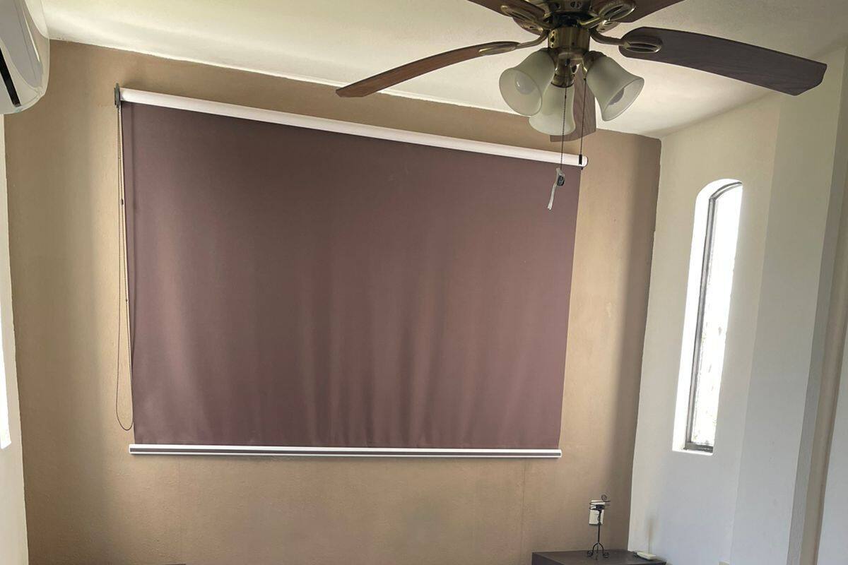 A bedroom with a bed, nightstands, a ceiling fan, a window, and a wall-mounted blind.