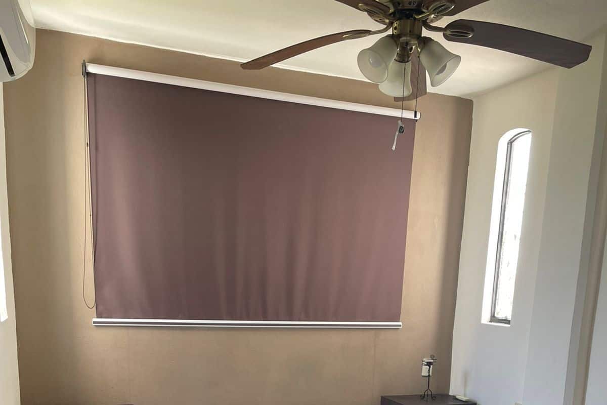 A bedroom with a bed, nightstands, a ceiling fan, a window, and a wall-mounted blind.