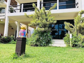 Un edificio con estructura de dos pisos, un área de entrada techada y una estatua de una figura sobre un pedestal.