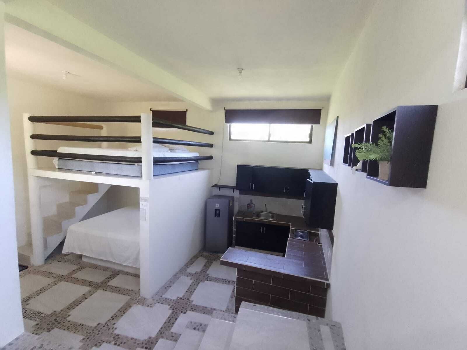 A compact room with bunk beds, a kitchenette, and a small window.