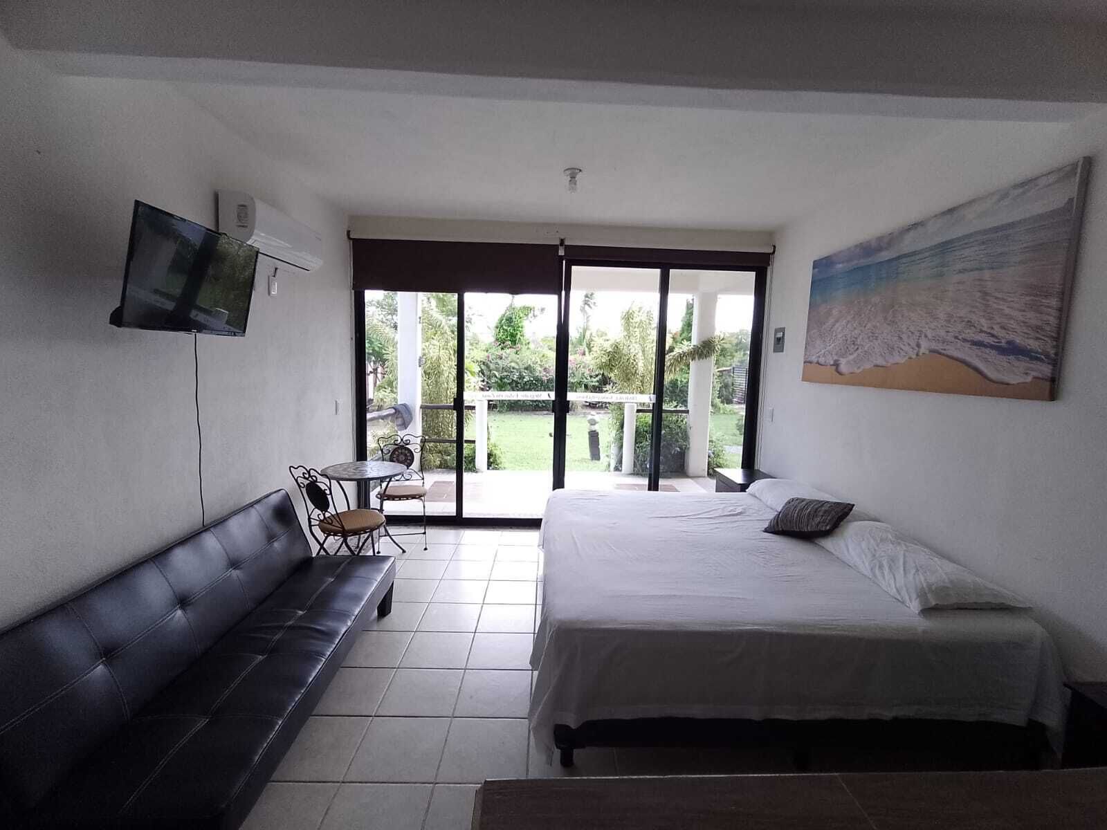 Ein Schlafzimmer mit Bett, einer Couch, einem Fernseher und einer Glastür, die auf einen Balkon führt.