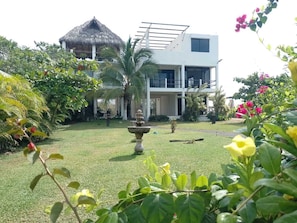 A modern building with a thatched-roof structure, a well-maintained garden with a fountain, and lush greenery.