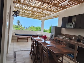An outdoor kitchen with a wooden table and chairs, a built-in microwave, and a view of the greenery. - Zana Town Bungalows (Barra de Potosi)