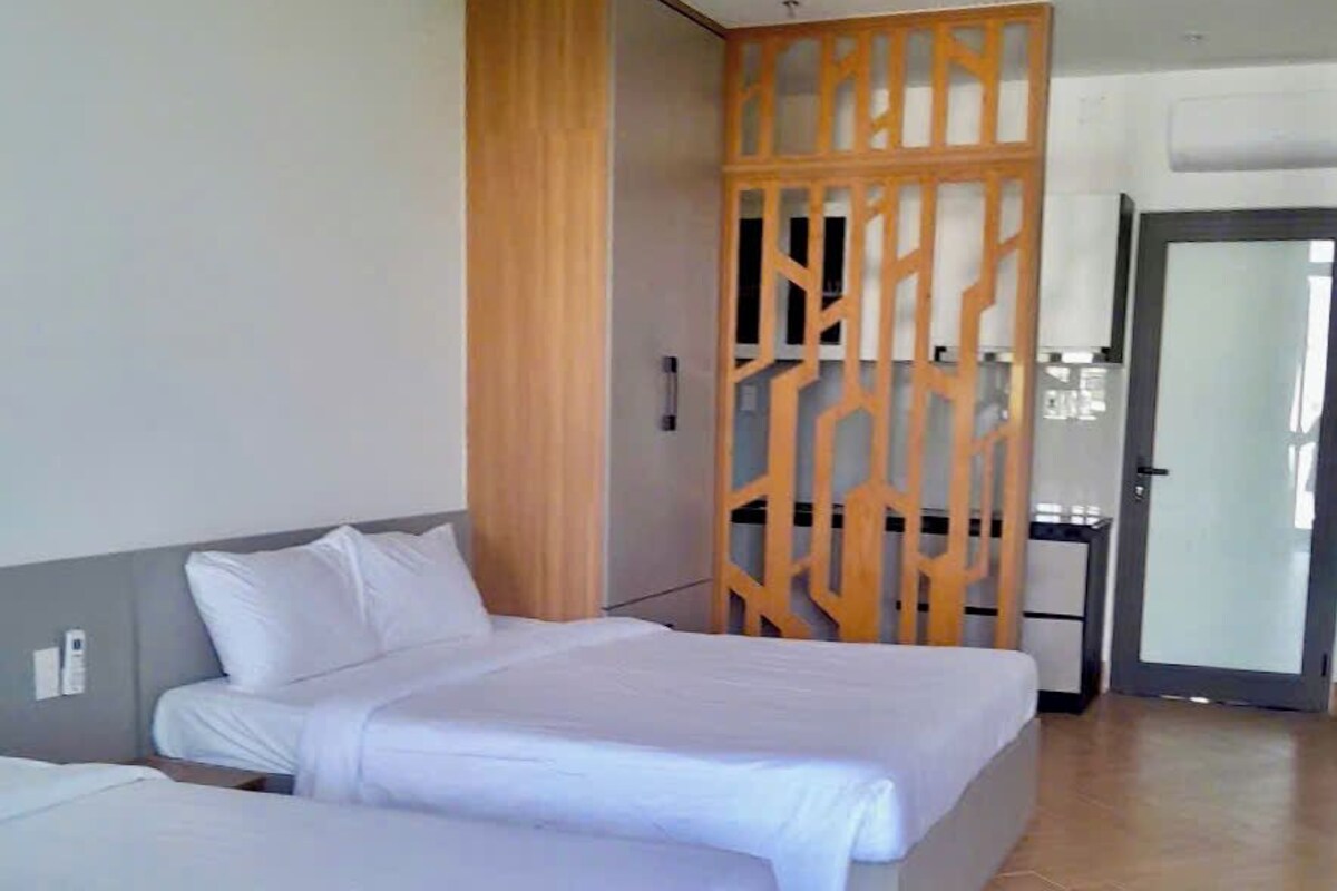 Une chambre d’hôtel avec deux lits, une cloison en bois, un bureau et une porte donnant sur un balcon.