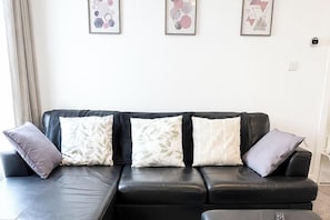 A black leather sofa with four cushions, a white wall, and three framed abstract artworks. - House Sleeps 7 with WiFi (Gateshead)