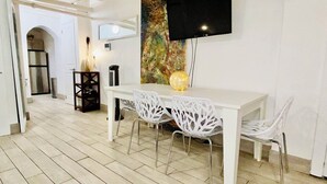 A dining area with a white table and chairs, a flat-screen TV mounted on the wall, and a decorative piece above the table. - THE BEST WEST VILLAGE APARTMENT (New York)