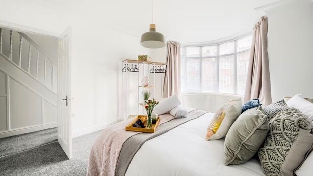 A bedroom with a bed, a bedside table, a hanging light, a window with curtains, and a staircase. - Coventry Sleeps 8 Garden and Large Driveway (Coventry)