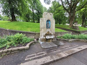 Een stenen monument met een standbeeld, omringd door groen en een geplaveid gebied met trappen.