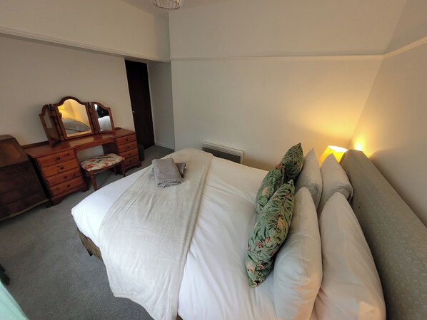 Een slaapkamer met een bed, een dressoir, een spiegel en een nachtkastje met een lamp.