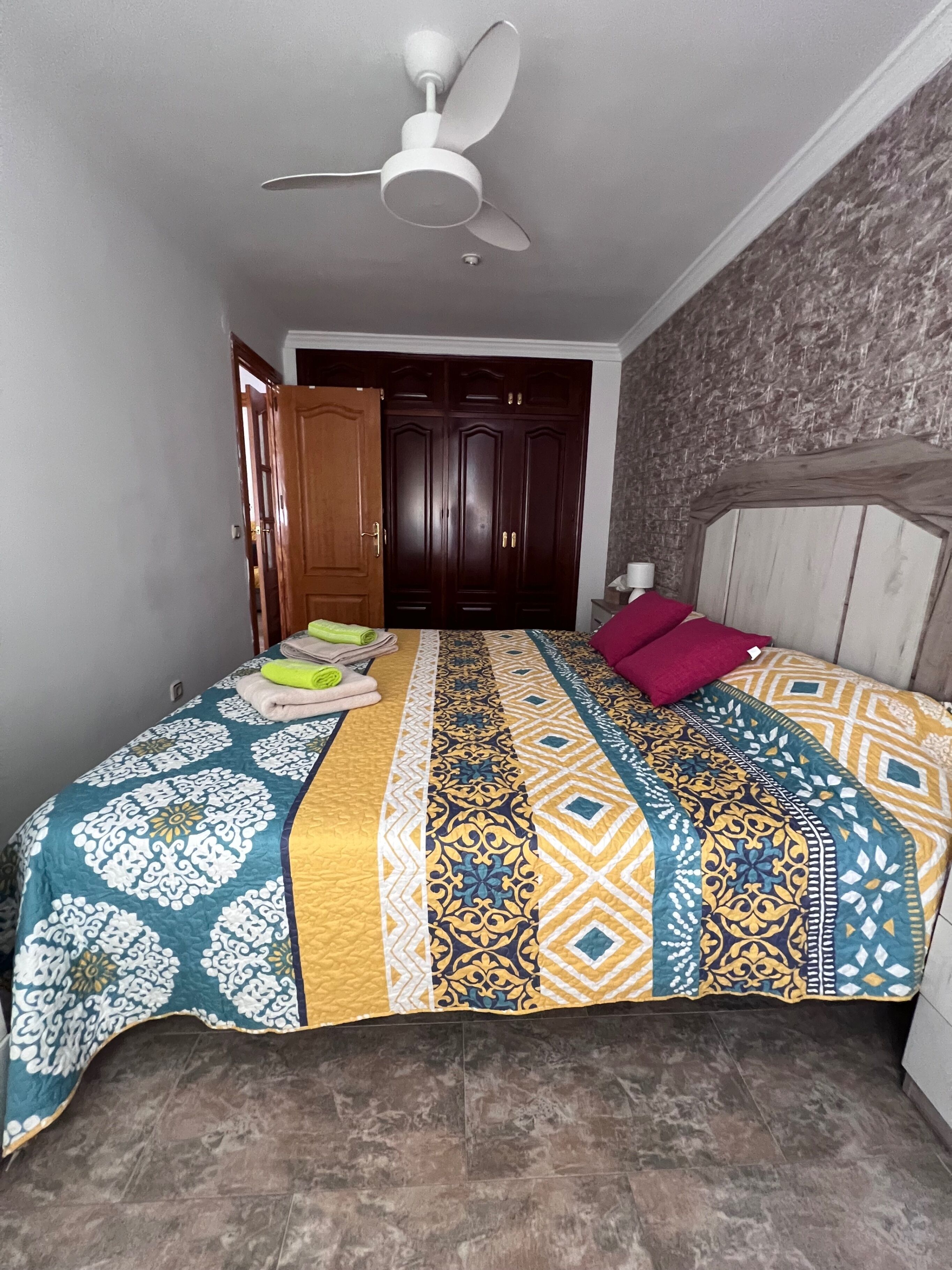 Une chambre à coucher comprenant un lit, un ventilateur de plafond, une armoire et une porte donnant sur une autre pièce.