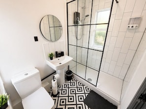 Ein Badezimmer mit Toilette, Waschbecken, Spiegel, Dusche und einem gemusterten Boden.