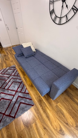 A room with a sofa bed, a patterned rug, wooden flooring, and a wall clock.. Erskine - House - Sleeps 4 - Parking - River Side