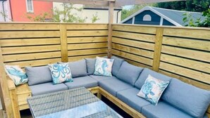 Um deck de madeira com um sofá modular e uma mesa estampada.